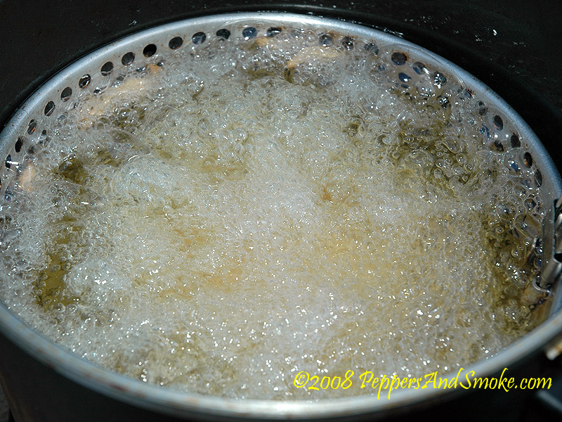 Battered bacon burger frying in a pot of oil