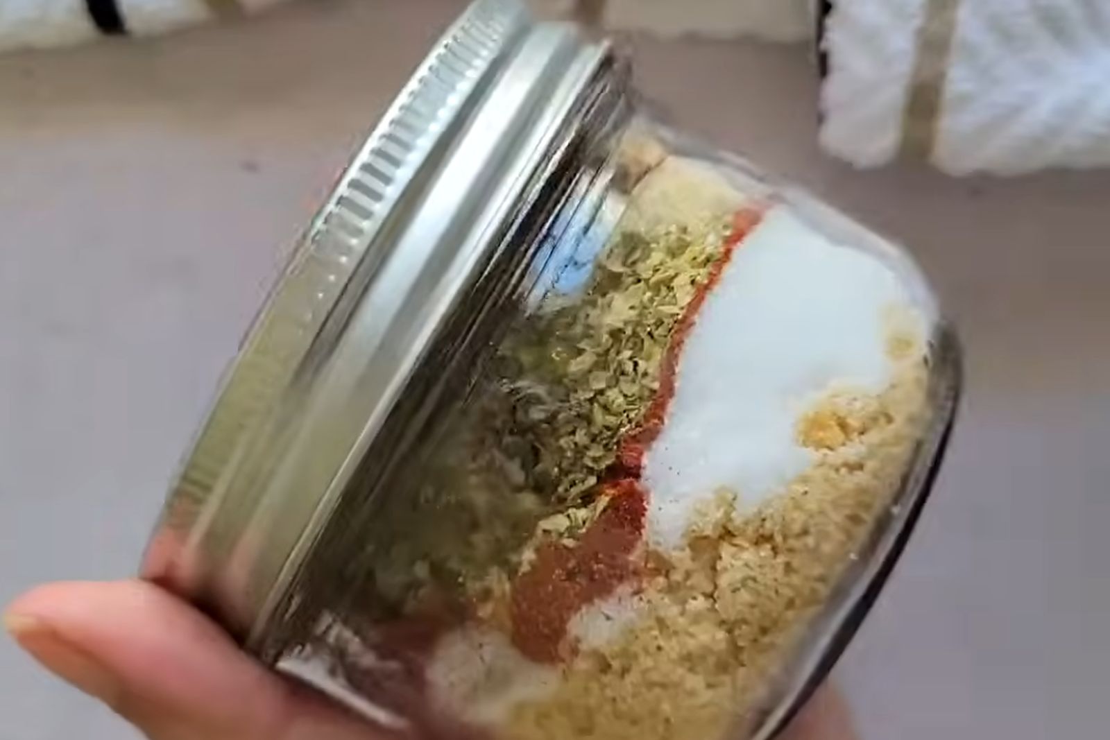 A glass mason jar of layered rub spices, held on its side with the lid on