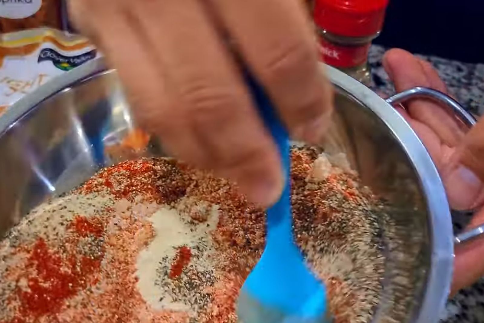 Mixing paprika, sugar, garlic powder and black pepper together in a stainless steel bowl with a blue spatula